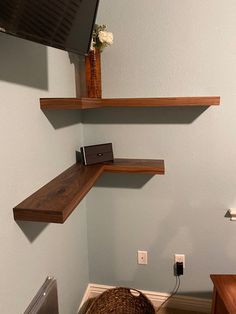 there is a tv mounted on the wall above some shelves in this small room with a wicker basket