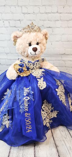 a teddy bear dressed in a blue dress with gold trimmings and a tiara