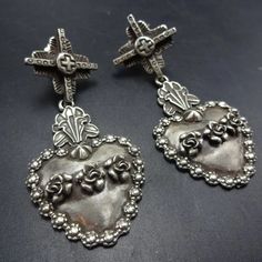 GREGORY SEGURA SOUTHWEST SANTA FE ARTISAN STERLING SILVER EARRINGS DESCRIPTION:  Solid sterling silver hearts adorned and framed with flowers hang from Tesuque crosses. These magnificent earrings by celebrated Santa Fe silversmith Gregory Segura will be a cherished addition to your collection of quality Southwestern and Native American jewelry. MEASUREMENTS: Earrings measure 2 3/8" x 1" WEIGHT: 24.2 grams SIGNED:  Gregory Segura  STERLING:  yes, stamped STERLING Traditional Silver Heart Earrings, Basket Earrings, Cowboy Jewelry, Silver Cross Earrings, Jewelry Measurements, Mexican Silver Jewelry, Funky Jewelry, Denver Co, Gothic Jewelry