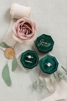 three green velvet ring boxes with wedding rings on them and a pink rose in the middle