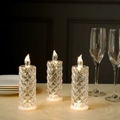 three lit candles sitting on top of a table next to wine glasses and silverware