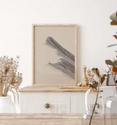 a table with vases and plants on it in front of a framed art piece