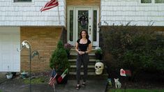 a woman standing in front of a white house with an american flag on the porch