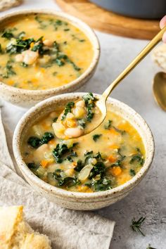 two bowls filled with soup sitting on top of a table next to bread and spoons