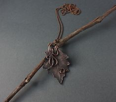 a leaf shaped pendant hangs from a twig on a gray surface with a chain attached to it