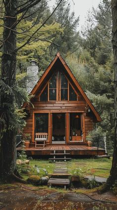 a log cabin in the woods surrounded by trees and grass, with two chairs on the porch