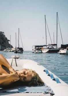 a woman laying on top of a boat in the ocean next to other boats and yachts