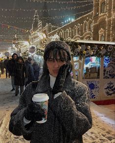 a woman standing in the snow talking on her cell phone and holding a cup of coffee