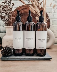 three bottles of shampoo sitting on top of a table next to a pine cone