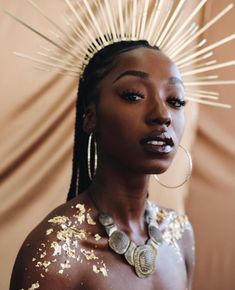 a woman with gold paint on her body and headdress in front of a wall