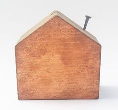 a wooden house with a nail stuck in the top of it's roof, against a white background