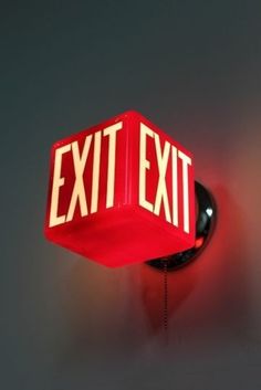 a red exit sign mounted to the side of a wall next to a light bulb