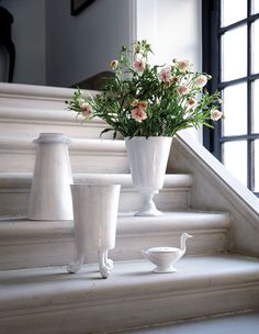 some white vases sitting on the steps with flowers in them