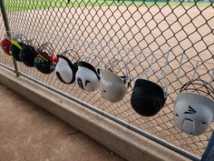 baseball helmets are lined up on the fence