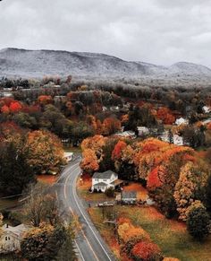 an aerial view of a road surrounded by trees with fall foliage on the mountains in the background