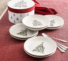 four white plates with christmas trees on them next to a red box and spoons