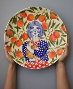 two hands holding a plate with an image of a woman and a cat on it