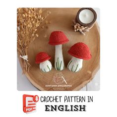 three crocheted mushrooms sitting on top of a wooden plate next to a candle