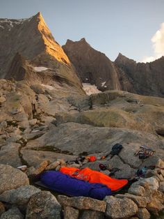 an orange and blue sleeping bag sitting on top of a rocky hill next to a mountain