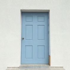 a blue front door sitting on the side of a white wall next to a cat