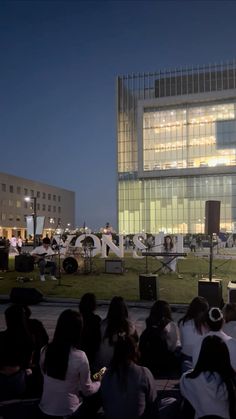 a group of people sitting on the ground in front of a large building at night