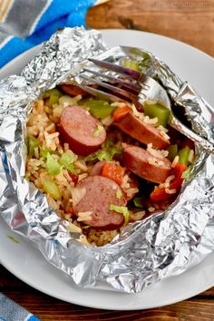 a white plate topped with sausage and rice covered in aluminum foil next to a fork