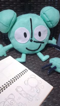 a green stuffed animal sitting on top of a table next to a notebook and pen