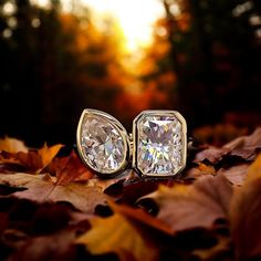 two diamond studs sitting on top of leaves in the sunlit forest at sunset