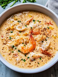 a bowl of soup with shrimp and garnishes on the top, sitting on a table