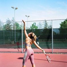 a woman holding a tennis racquet on top of a tennis court in front of a fence