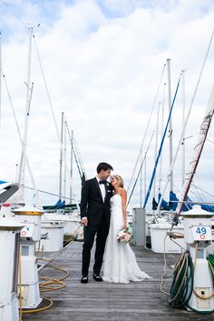 a bride and groom standing on a dock in front of sailboats