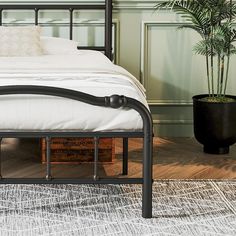 a black metal bed frame with white sheets and pillows on top of a wooden floor next to a potted plant