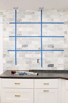 a kitchen counter with blue tape on the backsplash and white cabinets in front of it