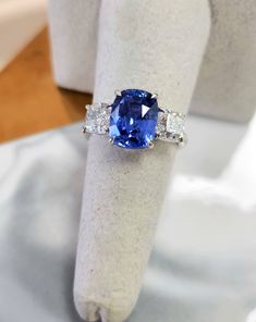 This is a truly regal ring, featuring a remarkably clean sapphire with a striking pop of blue. This vivid crystal blue, natural sapphire hails from Ceylon, Sri Lanka. The sapphire, in a gorgeous cushion shape, is complemented by diamond accent square cushions, all set in 18 Karat white gold. Perfect as an engagement ring or an anniversary gift, its beauty and uniqueness are unparalleled. The stones are securely low-set in claw prongs, imparting an antique feel and energy to the ring. The ring comes with a certificate from AGL Thai Laboratory, noting its vivid blue color, transparency, and indication of heating (a very common treatment). The diamonds weigh approximately 1 carat each, 2 carats total weight. Both colorless and very clean. (G/H VS/SI) The ring is size 6.5, but can be resized u Luxury Sapphire Gemstones With Brilliant Cut, Luxury Brilliant Cut Sapphire Gemstones, Blue Sapphire Gemstone Ring In Platinum, Platinum Blue Sapphire Gemstone Ring, Luxury Sapphire Gemstones With Round Cut, Luxury Blue Sapphire Ring Gia Certified, Luxury Blue Sapphire Platinum Ring, Luxury Royal Blue Sapphire Ring With Diamond, Blue Brilliant Cut Gemstones For Formal Occasions