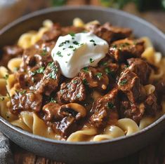 a bowl filled with pasta and meat covered in sauce, sour cream and parsley