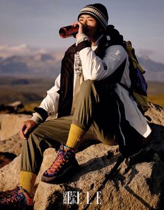 a man sitting on top of a large rock drinking from a bottle while wearing hiking gear