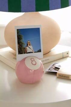 a pink ball sitting on top of a white table next to a lamp and photos