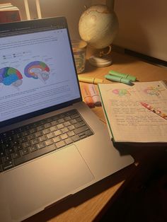 an open laptop computer sitting on top of a wooden desk next to a notebook and pen