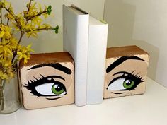 two bookends with eyes painted on them next to a vase with yellow flowers