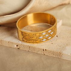 a close up of a gold colored bracelet on a piece of wood with a cloth in the background