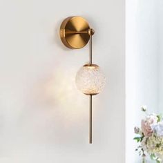 a white vase with flowers in it next to a gold wall mounted light on the wall