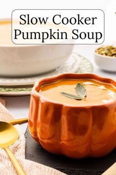 a bowl of slow cooker pumpkin soup on a table with spoons and bowls in the background