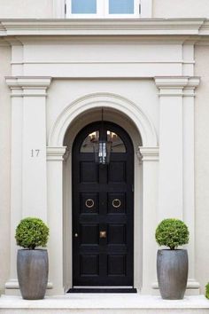 two large planters are in front of a black door on a beige building with white trim