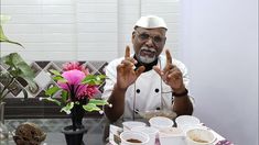 a man sitting at a table making the peace sign with his hands while holding up two fingers