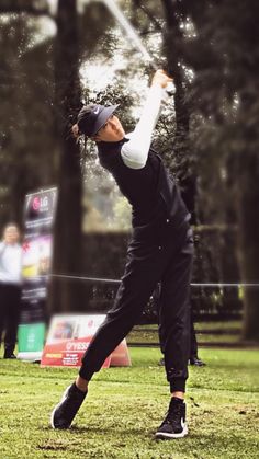 a man swinging a golf club on top of a lush green field in front of trees