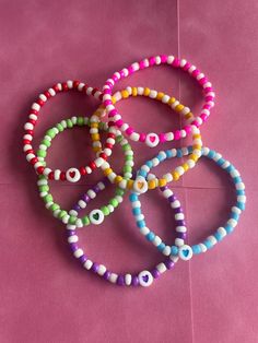 four bracelets with different colored beads on a pink surface