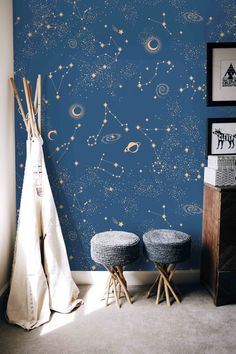 the wallpaper in this room is painted with stars and planets, while two stools are