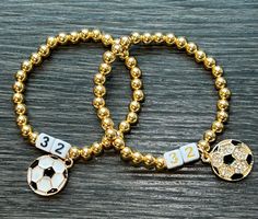 two gold beaded bracelets with soccer balls and numbers on them, sitting on a wooden surface