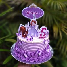 a hand holding a purple cake decorated with princesses and animals on it's top