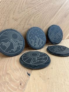 four black stones sitting on top of a wooden floor next to each other with designs painted on them